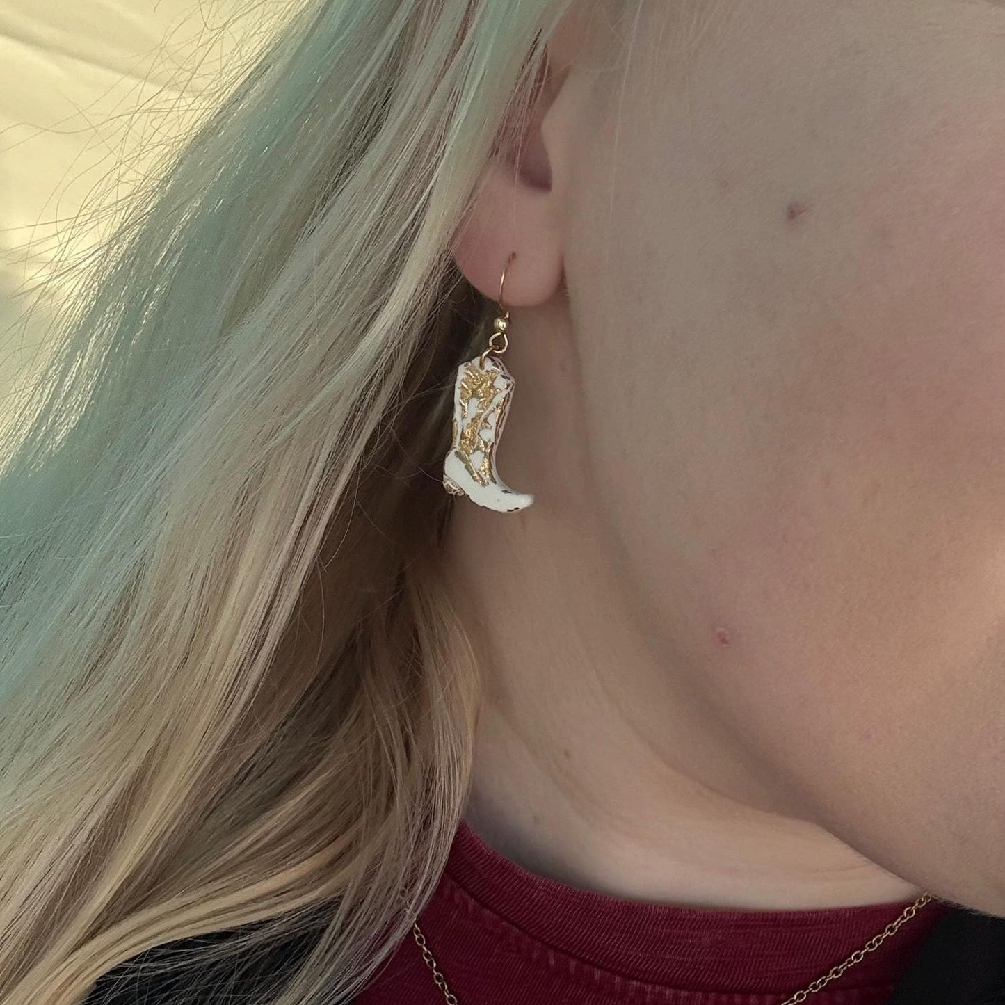 Close-up of a person wearing a cowboy boot earring and necklace.
