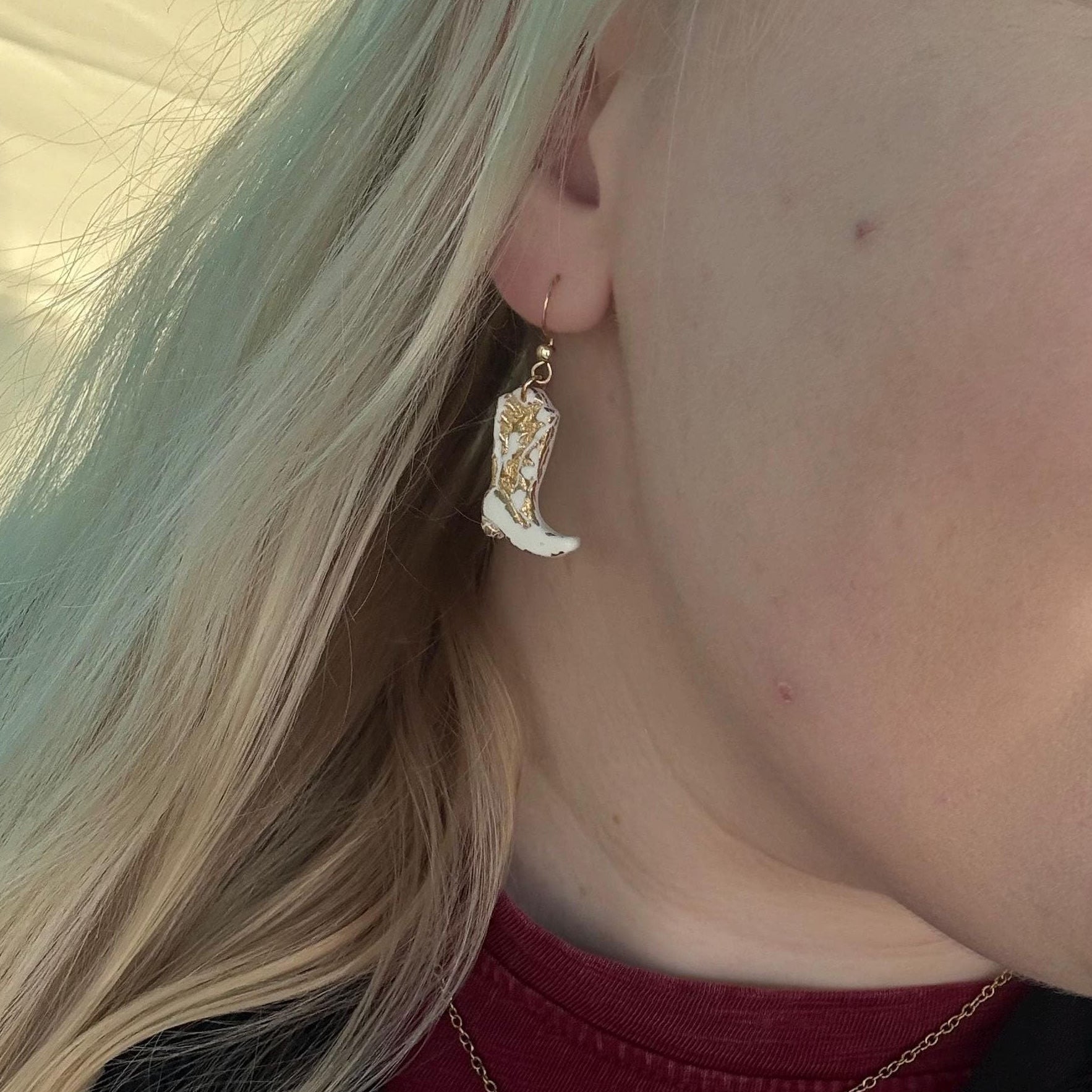 Close-up of a person wearing a cowboy boot earring and necklace.